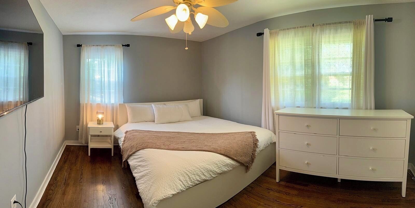 Une chambre à coucher comprenant un lit, une table de chevet, une commode et un ventilateur de plafond.