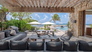 A covered outdoor seating area with a stone wall, a pool, and umbrellas.