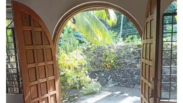 An open wooden door leading to a paved path with greenery outside.