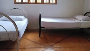 A room with two metal beds, a wooden floor, and windows with wooden frames.
