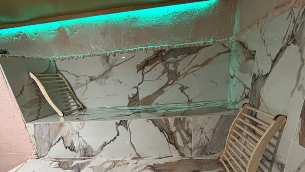 A bathroom with marble walls and a glass shower enclosure.
