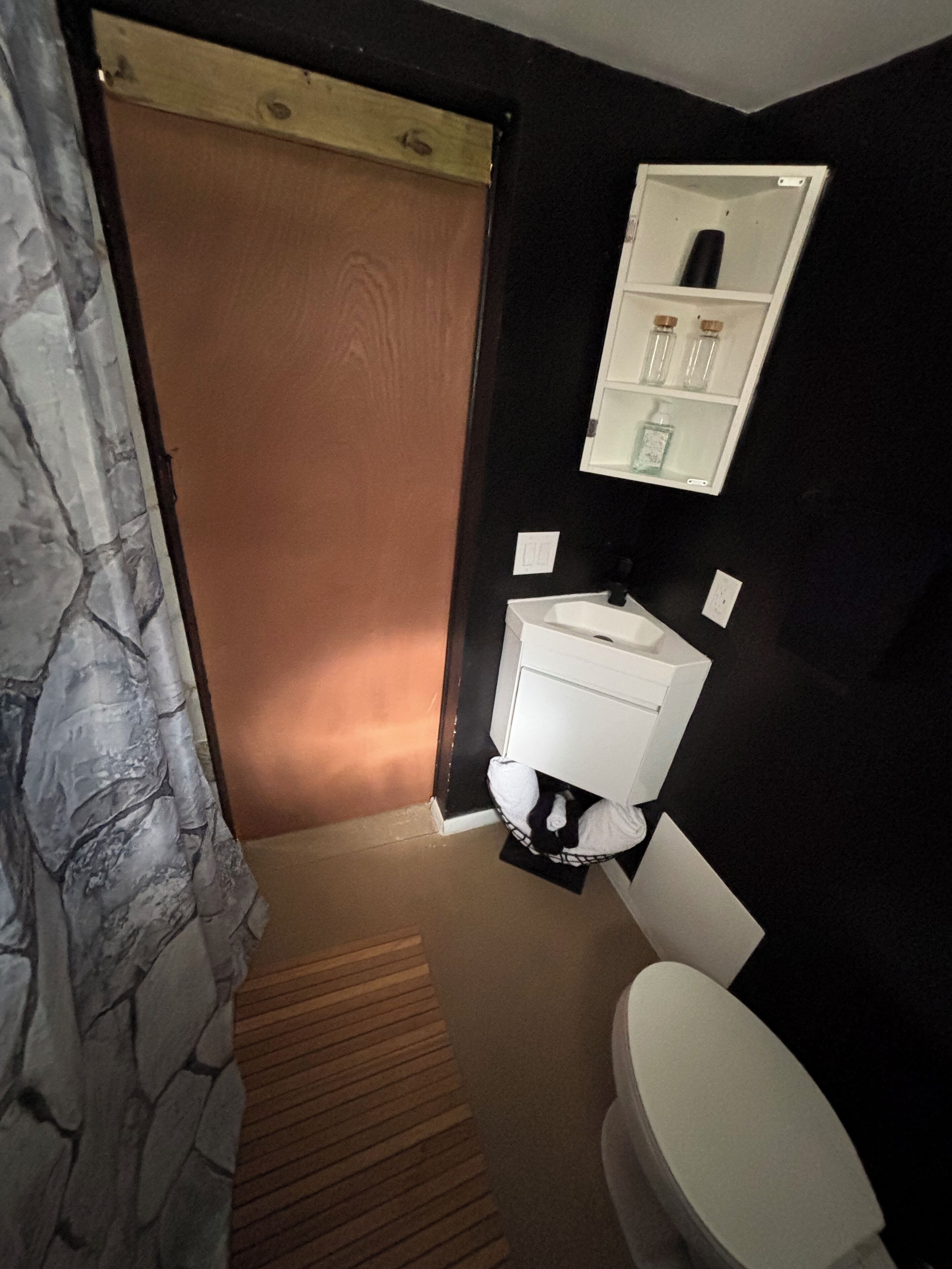 A bathroom with a white toilet, a sink, and a mirror above it. There is a wooden door leading to another room.