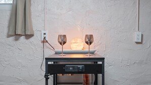 A table with two wine glasses and a candle, set against a textured wall with a power outlet and a cable.