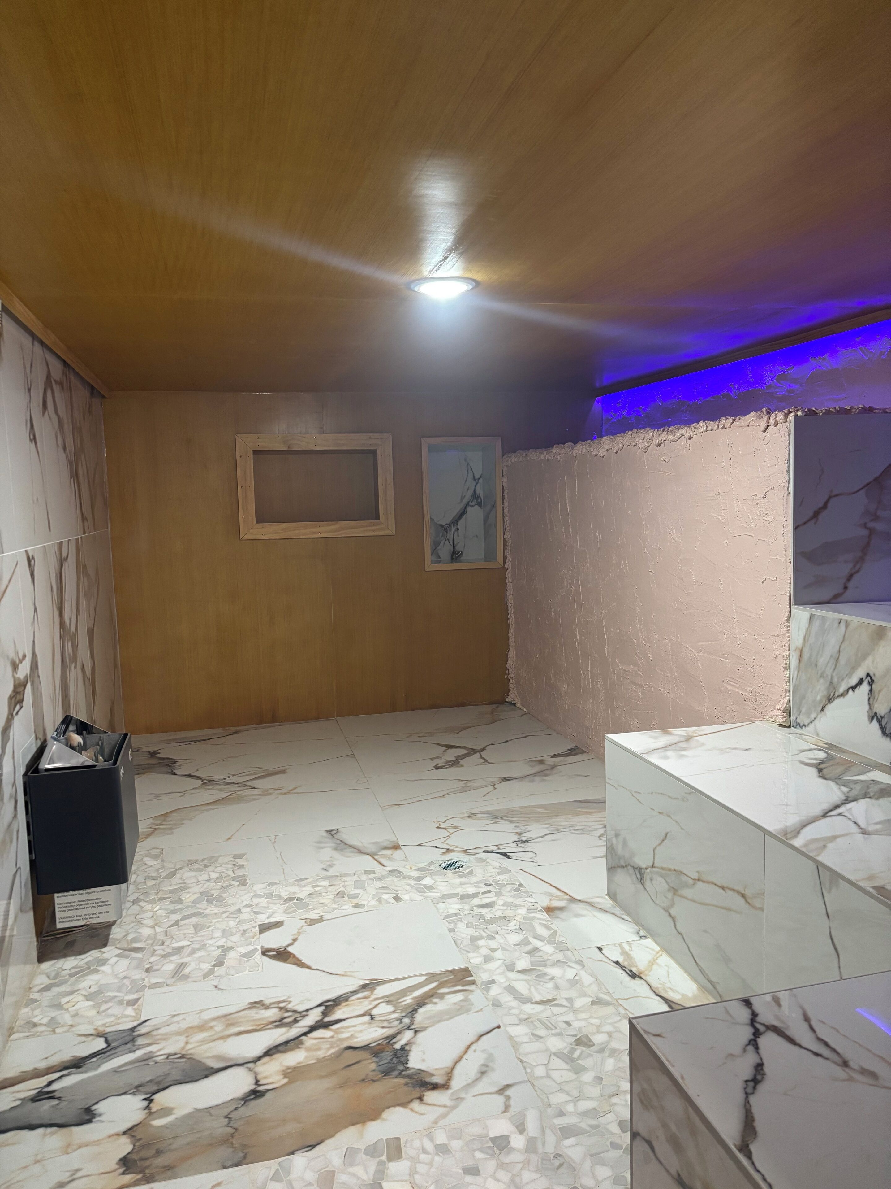 A room with a wooden ceiling, marble flooring, and a light fixture.