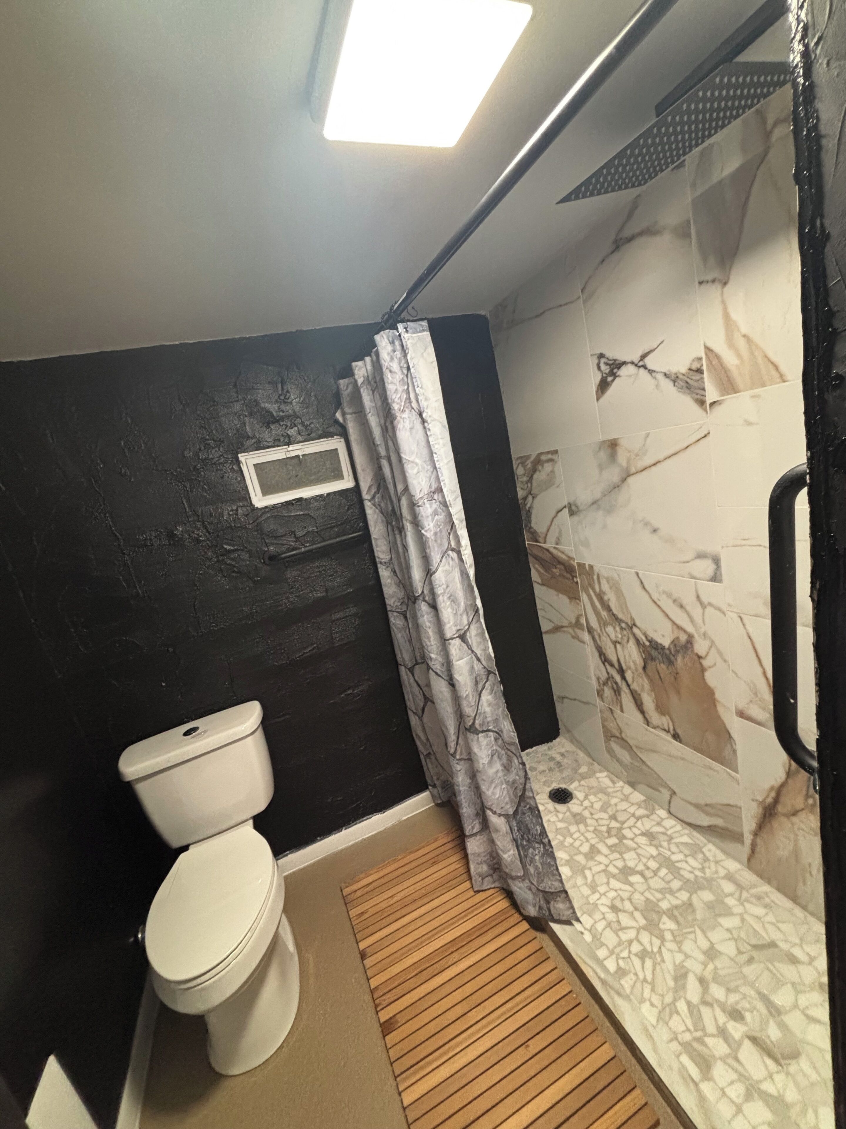 A compact bathroom with a toilet, a shower with a patterned curtain, and a tiled wall with a marble-like design.