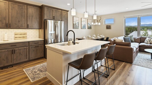 A modern kitchen with wooden cabinets, a stainless steel refrigerator, and a large island with bar stools.