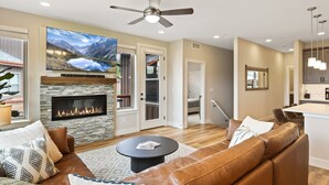 A modern living room with a fireplace, leather sofa, and a flat-screen TV mounted above it.