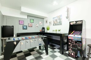 Une pièce équipée d’un baby-foot, d’une télévision et d’une borne d’arcade rétro.