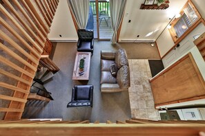 A spacious living area with a high ceiling, a wooden staircase, a leather sofa, a coffee table, and a view of the outdoors. - Bob's Sled Lodge – 2BR Killington Retreat Near Slopes & Trails (Killington)