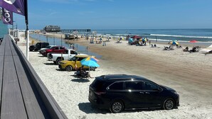 Una playa con un camino de madera, coches aparcados y sombrillas.