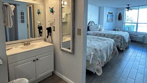 Un dormitorio con dos camas, un espejo grande, una tocador con lavamanos y un ventilador de techo.