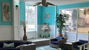 Una sala de estar con un sofá seccional grande, un ventilador de techo, un reloj y vistas al exterior.