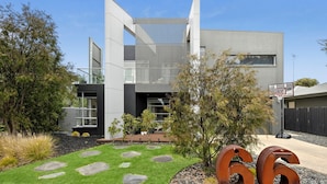 Een modern huis met twee verdiepingen, minimalistisch vormgegeven, met een groot raam en een basketbalring in de achtertuin.