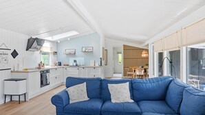 A modern living room with a blue sofa, a coffee table, and a kitchen in the background. - Stunning home in Væggerløse with WiFi (Væggerløse)