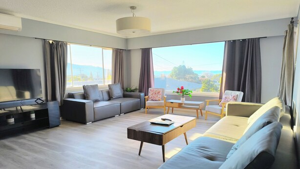 Una sala de estar moderna con un sofá modular, un televisor de pantalla plana, una mesa de centro y vistas al exterior.