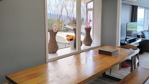 Un comedor moderno con una larga mesa de madera, bancos y jarrones de mimbre decorativos con flores.