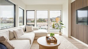 Una sala de estar moderna con un sofá grande, una mesa de centro y vistas a un paisaje urbano a través de amplios ventanales.