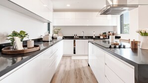 Una cocina moderna con armarios blancos, encimera negra y una isla central. Hay plantas y utensilios de cocina en la encimera.