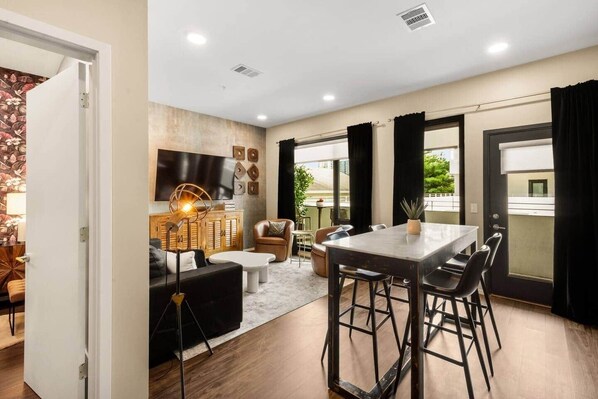 A modern living room with a flat-screen TV, a wooden cabinet, and a dining area with a table and chairs.