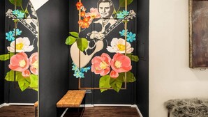 Ein Zimmer mit einer schwarzen Wand, die ein Wandgemälde eines Gitarristen inmitten von Blumen zeigt. Es gibt eine Bank und einen mit Fell bezogenen Sessel.