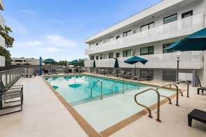A swimming pool with lounge chairs and umbrellas, surrounded by a building with a modern design.
