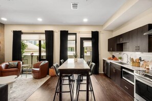 A modern kitchen with dark cabinets, a stainless steel oven, and a dining area with a table and chairs.