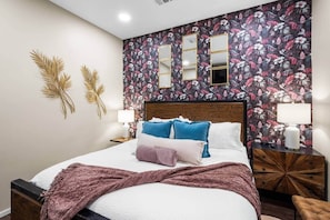 A bedroom with a floral wallpaper, a wooden headboard, two bedside tables with lamps, and a bed with multiple pillows.