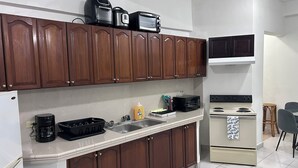 Une cuisine avec des meubles de rangement en bois, un plan de travail blanc, une machine à café, un four à micro-ondes et une cuisinière.