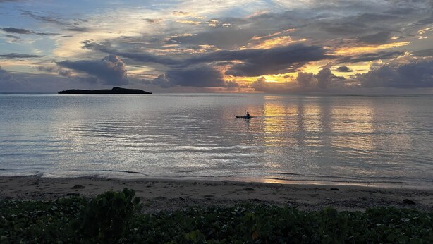 Une mer calme, un bateau, une île lointaine et un ciel nuageux.