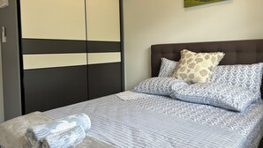 Une chambre à coucher avec un lit, des oreillers, une couverture, une armoire et un tableau accroché au mur.