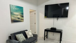 Un salon avec un canapé gris, un meuble TV noir et un téléviseur fixé au mur.