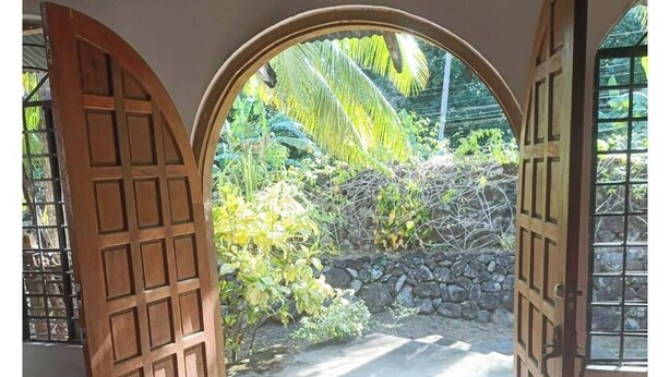 An open wooden door leading to a paved pathway with a stone wall and greenery. - Monte Carlo Camiguin Ruins, Looc Catarman Camiguin (Catarman)