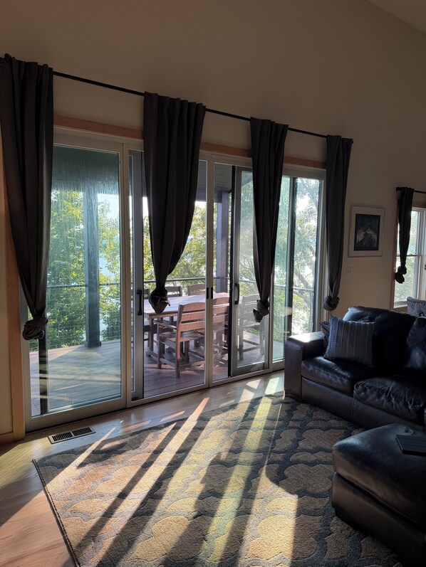 Un salon doté d’une porte-fenêtre coulissante donnant sur une terrasse extérieure, d’un canapé en cuir et d’un tapis à motifs.