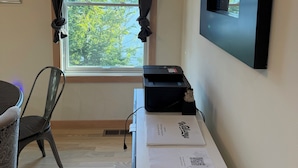 Quarto com escrivaninha, cadeira, impressora e janela com cortinas.