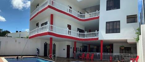 A multi-story building with a swimming pool, balconies, and red and white color scheme.
