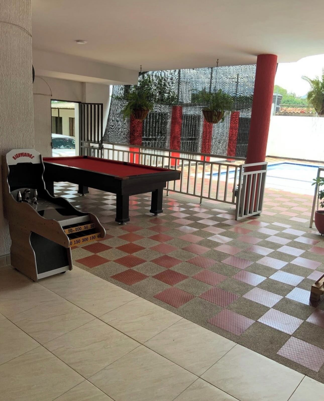 A billiards table with a checkered floor and a pool table in a covered area with a railing and potted plants.