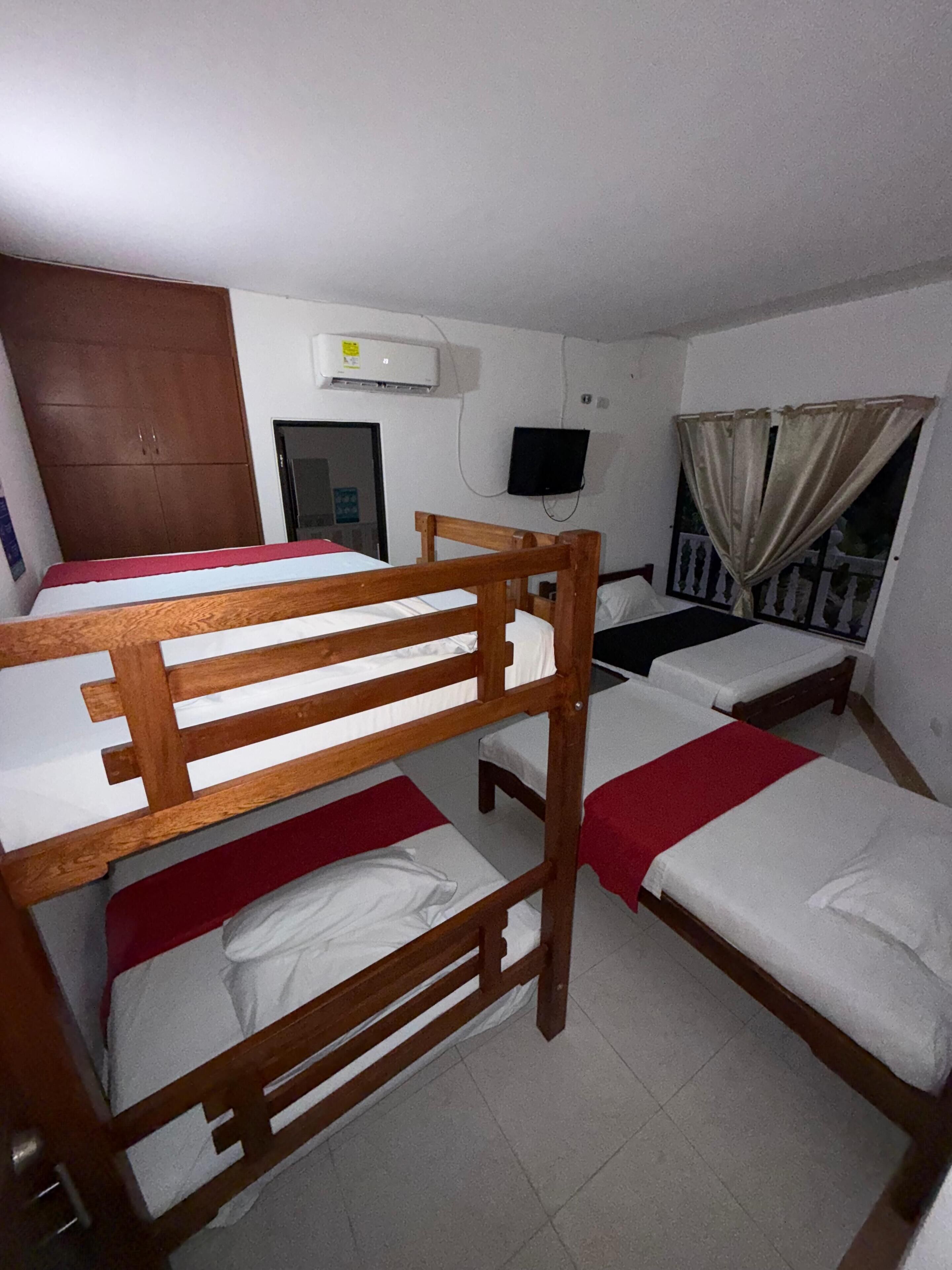 A dormitory room with bunk beds, a television, an air conditioning unit, and a window with curtains.