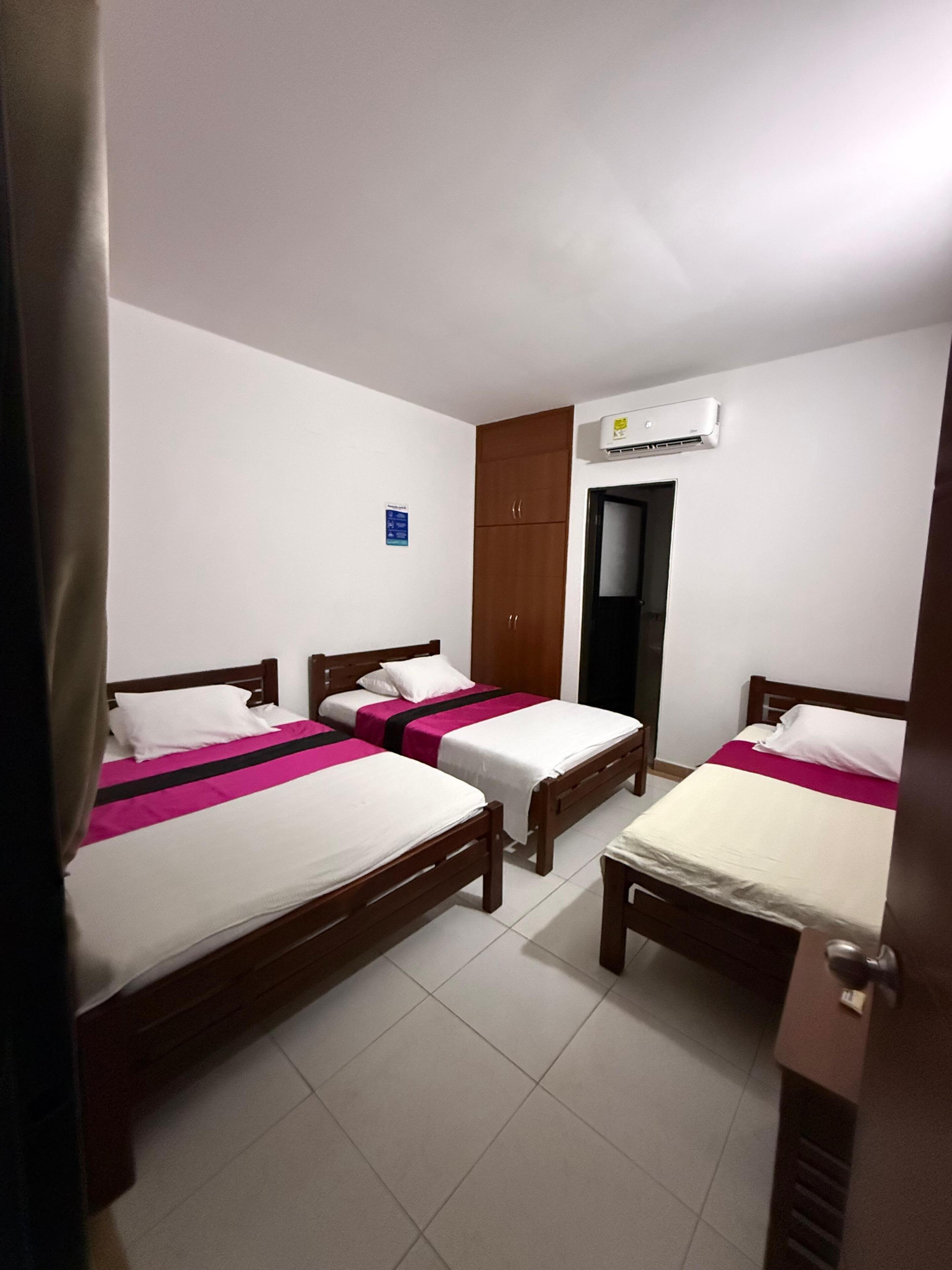 Une chambre avec trois lits simples, une armoire, un appareil de climatisation et une porte.