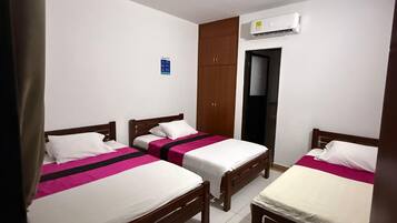 Une chambre avec trois lits simples, une armoire, un appareil de climatisation et une porte.