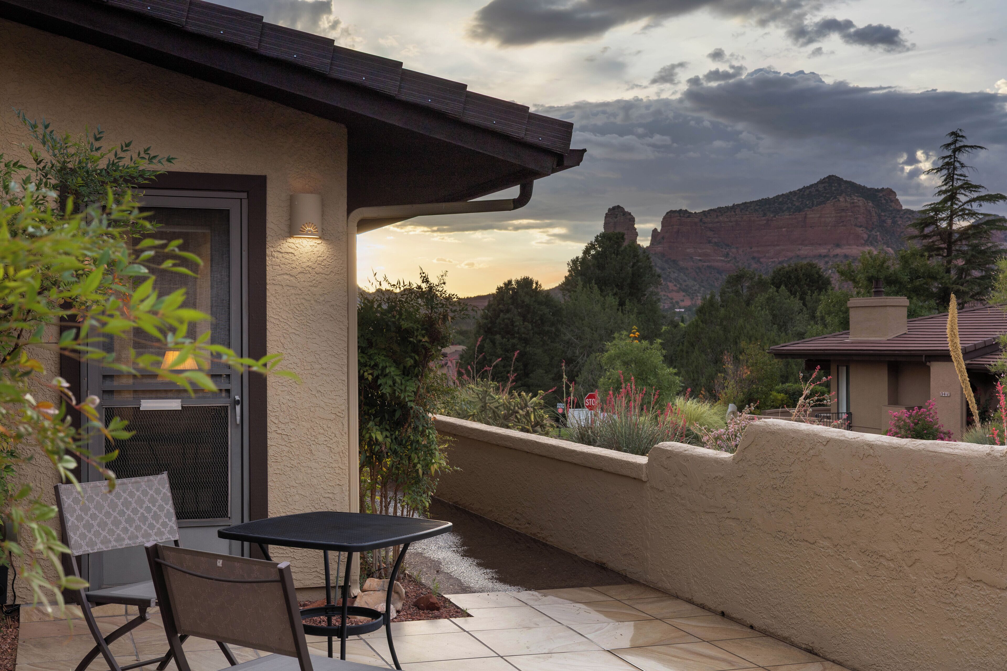 An outdoor patio with a table and chairs, a door with a screen, and a view of a mountain range.