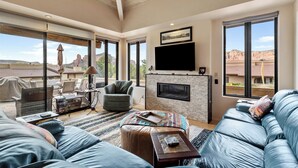 Un salón amplio con chimenea, ventanas grandes, ventilador de techo y una zona de estar confortable.