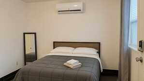 A modern bedroom with a bed, a mirror, an air conditioning unit, and a door with a curtain. - Modern Art Studio in the Heart of Wynwood (Miami)