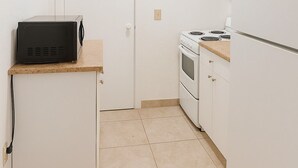 A compact kitchen with white cabinetry, a microwave, an oven, and a refrigerator. - Modern Art Studio in the Heart of Wynwood (Miami)