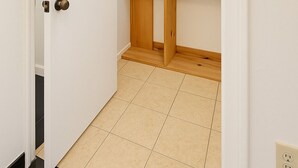 A hallway with a white door, a wooden closet with multiple shelves, and a tiled floor. - Modern Art Studio in the Heart of Wynwood (Miami)