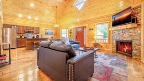 A cozy log cabin interior with a living room, kitchen, and fireplace. - Dancing Bear Hideaway - Hot Tub, Resort Pool & Wooded Mountain Retreat (Gatlinburg)