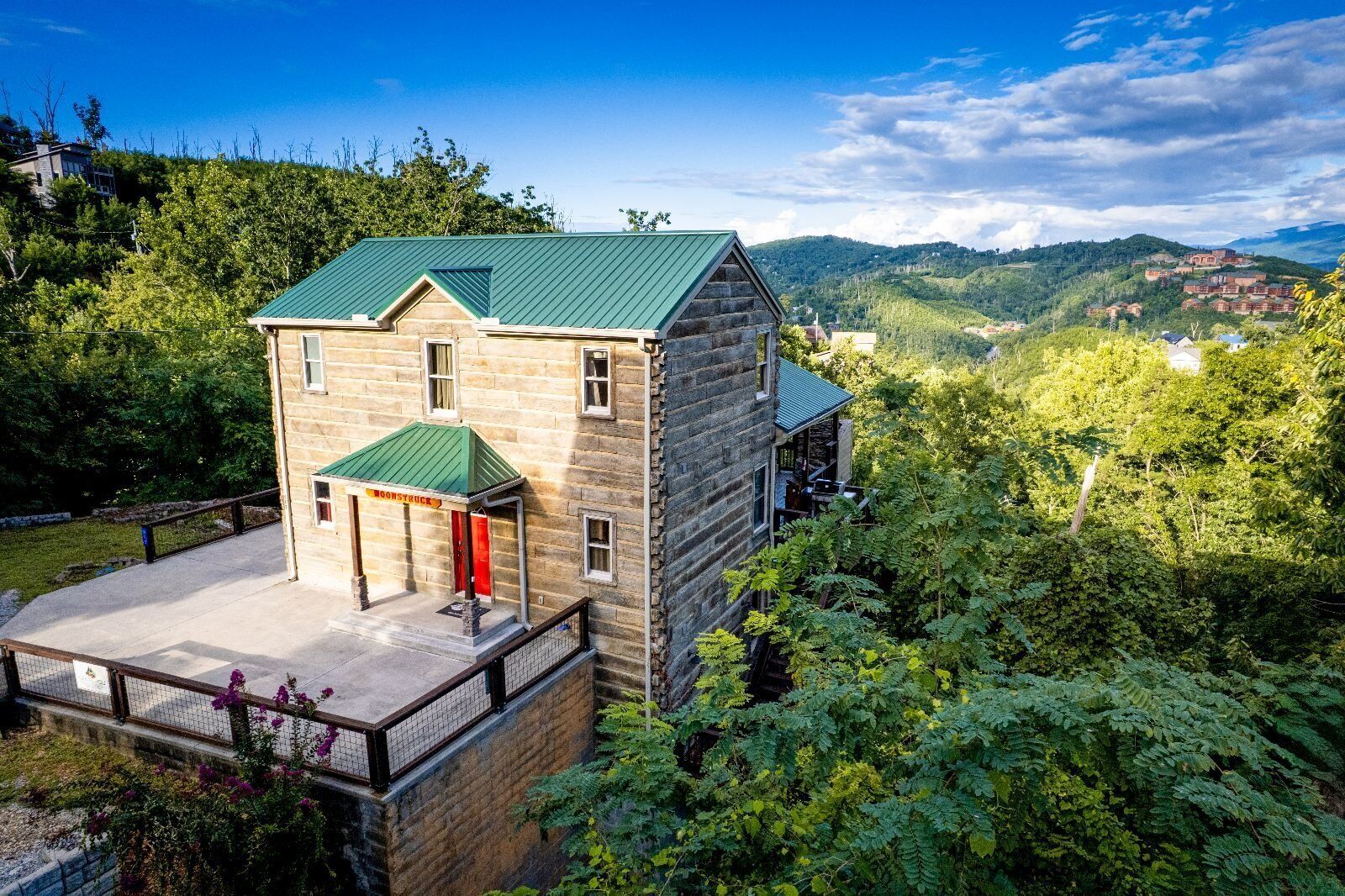 A two-story stone building with a green roof, a red door, and a small porch area.