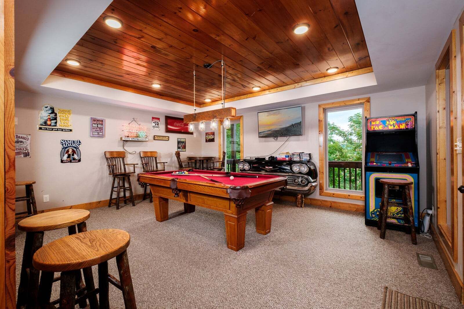 Ein Billardtisch in einem Raum mit Holzbalkendecke, Barhocker, Spielautomaten und einem Bild an der Wand.