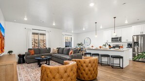 A modern living room with a sectional sofa, a coffee table, and a rug. There is a kitchen area with white cabinets, a microwave, and a refrigerator. - Skyline 1634, Private Swim Spa & Hot Tub (Washington)