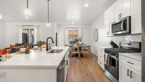 A modern kitchen with white cabinets, stainless steel appliances, a central island, and wooden flooring. - Skyline 1634, Private Swim Spa & Hot Tub (Washington)