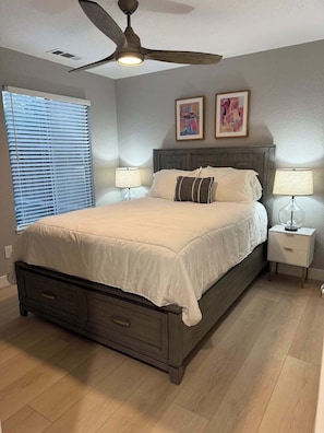 A bedroom with a bed, two nightstands, a ceiling fan, and a window with blinds.